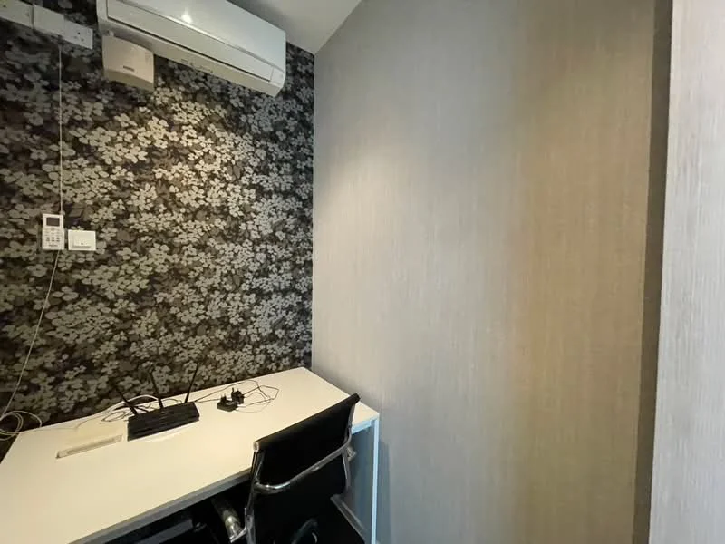 Study features: black floral wallpaper, light wood paneling, white desk, black office chair, wall-mounted air conditioning unit, electrical outlets, cable management, desk with keyboard and mouse; style: modern.