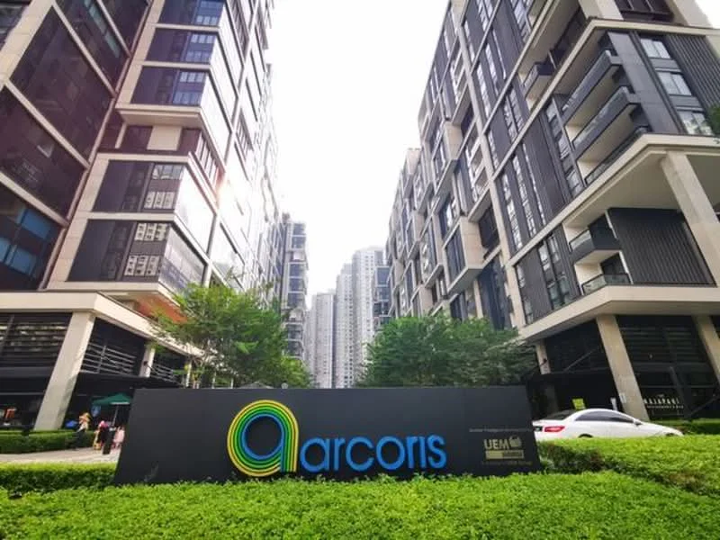 Exterior type: mid-rise condominium; features: modern facade with glass and concrete, landscaped garden with greenery, prominent signage, multiple balconies, surrounded by urban skyline, well-maintained entrance area; style: modern.