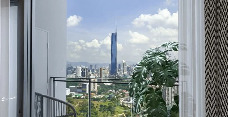 Room features: floor-to-ceiling windows, glass balcony railing, city skyline view, greenery visible outside, plant in pot; style: modern; view: city.