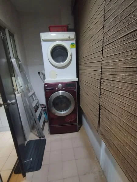 Laundry features: front-load washing machine in white, front-load dryer in red, tile flooring, blinds on window, ladder, shelf above appliances, wall-mounted electrical outlet.