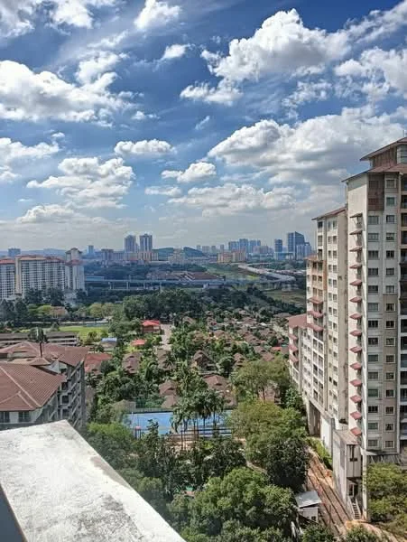 Exterior type: high-rise condominium; features: city skyline view, surrounded by greenery, near residential area, multiple high-rise buildings in the background, clear blue sky, scattered clouds; style: modern.