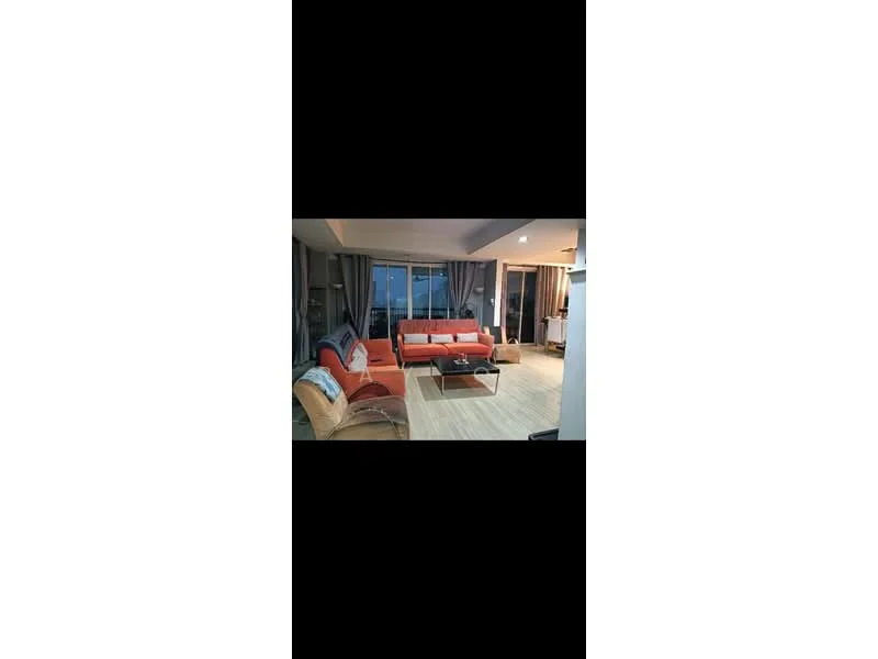 Living features: 3-seater fabric sofa in orange, 2-seater fabric sofa in beige, coffee table with wooden top, area rug with geometric pattern, floor-to-ceiling windows, sheer curtains, wooden flooring, recessed downlights, decorative cushions, wall-mounted TV, entertainment unit; style: modern; view: city.
