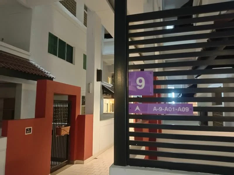 Exterior type: low-rise apartment block; features: white painted facade, red accent wall, metal railing, staircase, numbered signage, intercom panel at entrance, covered walkway, green windows; style: modern.