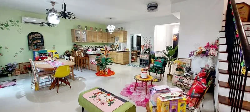 Living features: 5-blade ceiling fan with light, wall-mounted split AC, white painted walls, cream tiled flooring, area rug with floral pattern, sofa with colorful upholstery, coffee table, decorative plants in pots, wall-mounted artwork, dining table with colorful chairs, kitchen area with wooden cabinetry, open shelving with decorative items, staircase with wooden railing; style: modern.