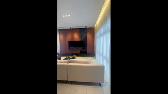 Living features: white leather sofa, wall-mounted TV, wooden feature wall, recessed lighting, large windows with sheer curtains, light-colored tiled flooring, decorative items on the coffee table, built-in cabinetry; style: modern.