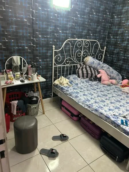 Bedroom features: metal bed frame with decorative headboard, mattress with floral bedding, striped and polka dot pillows, mirrored vanity table, makeup and personal items on table, plastic laundry basket, suitcases on the floor, white tiled flooring, grey pouf, slippers on the floor, dark patterned wallpaper, window with green frame.