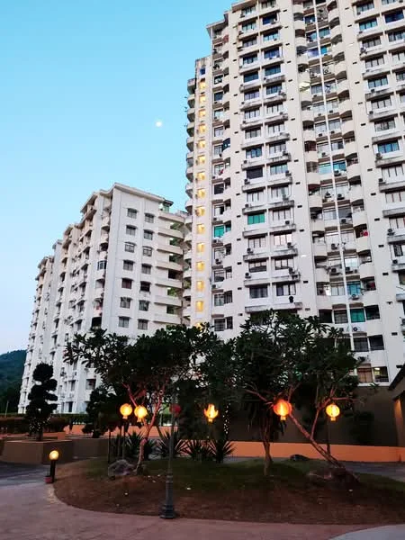 Exterior type: mid-rise condominium; features: white painted facade, balconies on each floor, landscaped garden with trees, pathway with decorative lighting, surrounding greenery, multiple storeys, evening lighting, mountain view in background; style: modern.