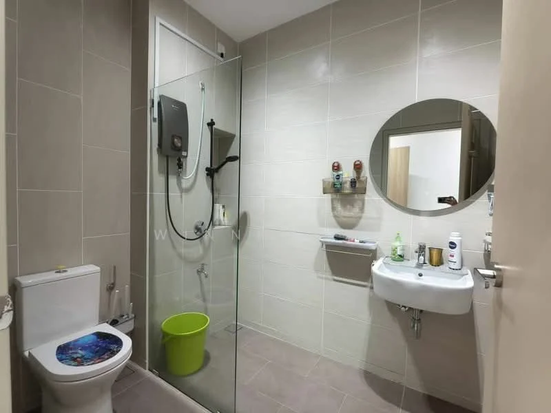 Bathroom features: walk-in shower with glass enclosure, chrome handheld shower, wall-mounted water heater, white sink with chrome faucet, round mirror, one-piece toilet, grey ceramic tile flooring, light beige wall tiles, green bucket, shelf with toiletries; style: modern.