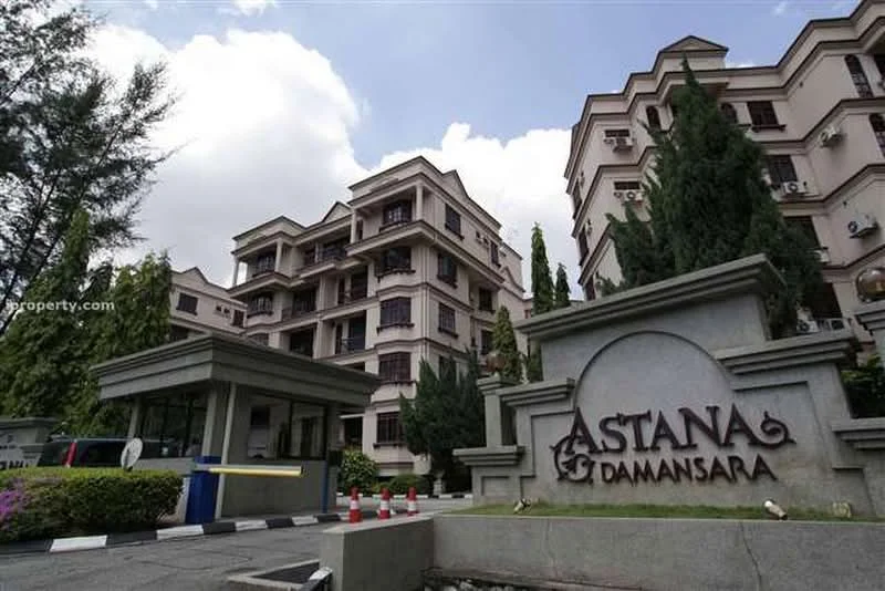 Exterior type: low-rise apartment block; features: cream painted facade, multiple storeys, landscaped garden with mature trees, security guardhouse at entrance, paved driveway, signage with 'ASTANA DAMANSARA', visible air conditioning units, surrounded by greenery; style: modern.