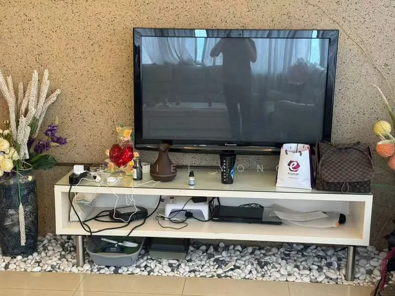 Living features: flat-screen TV on console, white console table, decorative pebbles under console, decorative flowers in vase, various bags on console, remote control, cable management visible, light-colored tiled flooring, large windows with sheer curtains, neutral wall color; style: modern.