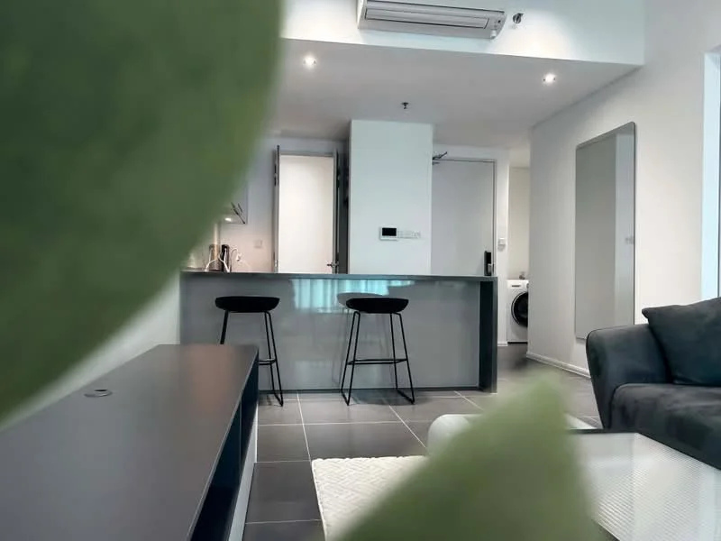 Living features: grey fabric sofa, coffee table, black bar stools, kitchen island with countertop, recessed downlights, wall-mounted air conditioning unit, floor-to-ceiling windows, tile flooring in dark grey, washing machine visible, mirror on wall; style: modern. Kitchen features: stainless-steel sink, chrome pull-down faucet, built-in oven, freestanding range oven, microwave, white cabinetry, grey countertop, open shelving; style: modern.