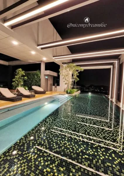 Exterior type: swimming pool deck; features: infinity pool, pool deck with loungers, mosaic tile flooring, landscaping with potted plants, ambient LED lighting, nighttime city skyline view; style: modern.