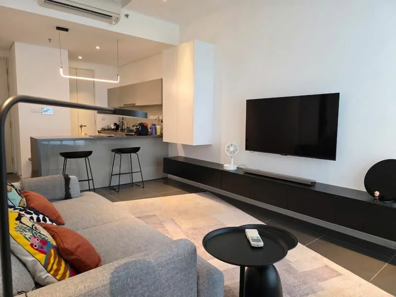 Living features: grey fabric sofa, colorful throw pillows, black coffee table, wall-mounted TV, TV console with storage, recessed ceiling lights, air conditioning unit, open kitchen layout, bar stools at kitchen counter, grey cabinetry, countertop with sink, kitchen appliances visible; style: modern.