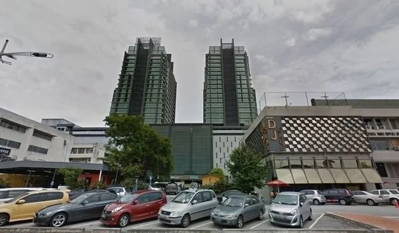 Exterior type: high-rise condominium; features: glass curtain wall, green facade, approximately 20-storey high-rise, surrounded by mature greenery, parking lot in foreground, adjacent commercial building, outdoor dining area, multiple balconies, feature lighting at night; style: modern.