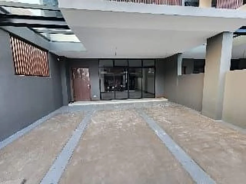 Exterior features: concrete flooring, grey painted walls, large glass windows, double-door entrance, open space layout, paved walkway, surrounding walls, overhead glass canopy; style: modern.