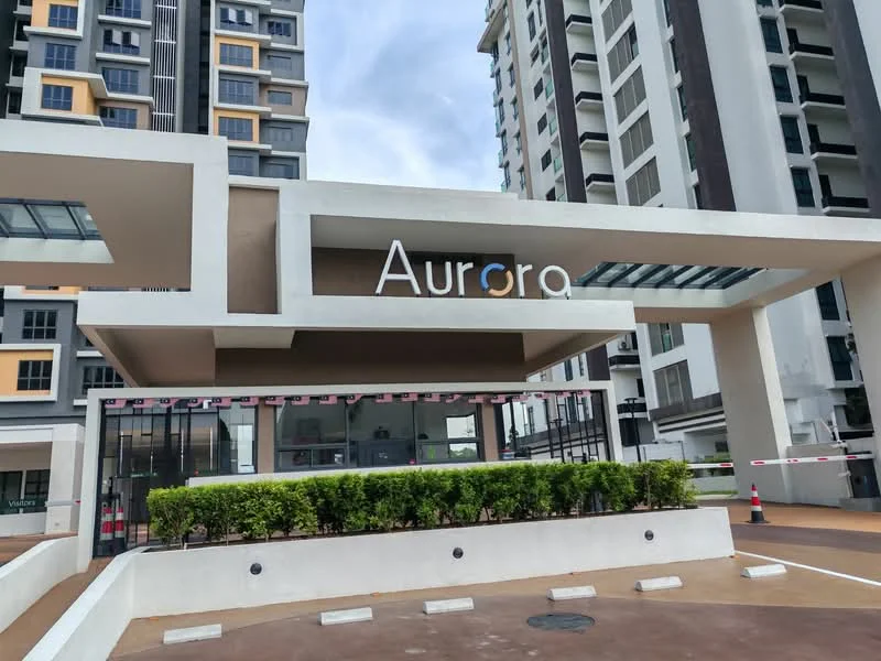 Exterior type: high-rise condominium; features: modern facade with large glass panels, prominent entrance with signage, landscaped greenery at entrance, guard house at entrance, paved driveway, surrounded by high-rise buildings; style: modern.