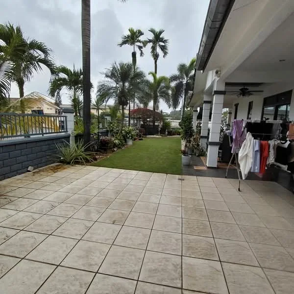 Exterior type: detached bungalow; features: paved patio area, manicured lawn, tropical landscaping, palm trees, garden area with plants, covered outdoor seating area, sliding glass door, exposed concrete wall, ceiling fan on patio, fenced perimeter; style: modern.