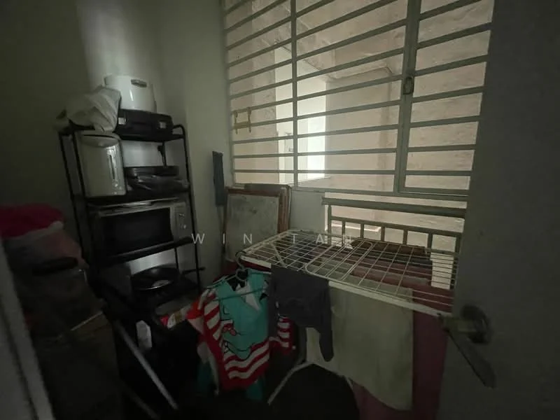 Room features: metal window grilles, clothes drying rack, stacked kitchen appliances, shelves, laundry items, light-colored walls, flooring not visible, natural light from window.