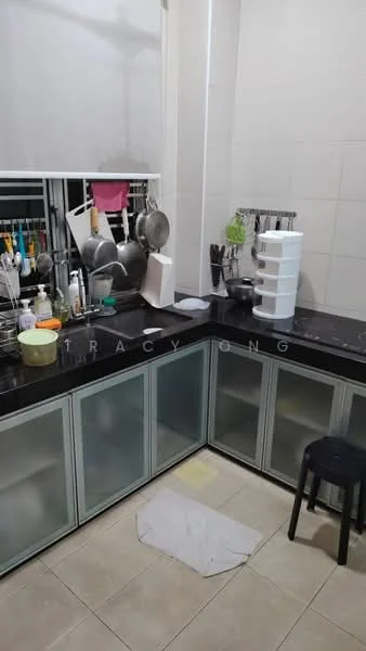 Kitchen features: black granite countertop, grey cabinetry with glass panels, stainless-steel sink, chrome faucet, kitchen utensils hanging on rack, stackable storage unit, ceramic tile flooring, window with sheer curtains, stool, cleaning cloth on floor; style: modern.