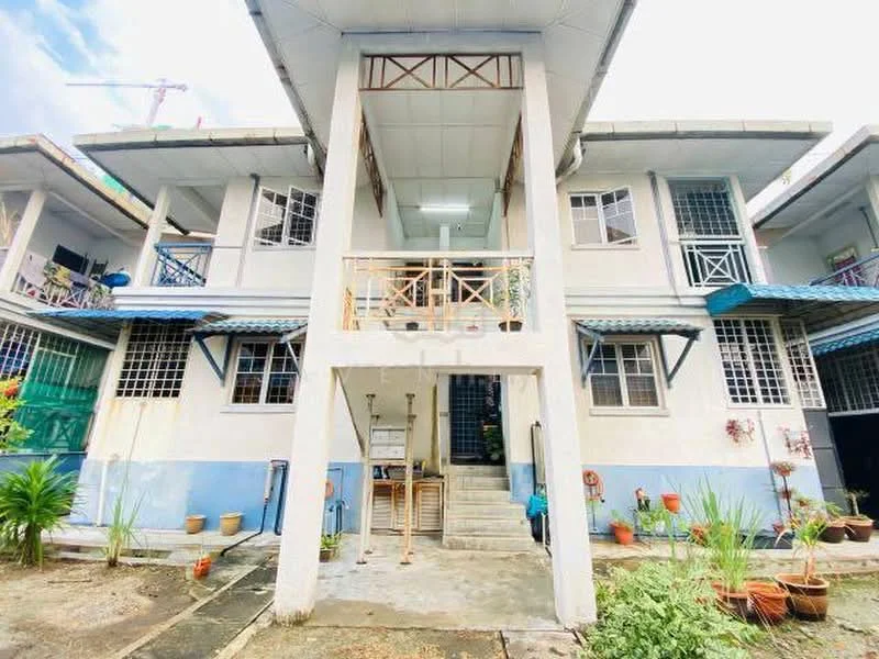 Exterior type: low-rise apartment block; features: two-storey building, balconies with railings, staircase leading to upper level, blue and white painted facade, multiple windows with grills, outdoor planters with plants, roof overhang, concrete flooring at entrance, visible construction crane in background; style: traditional.
