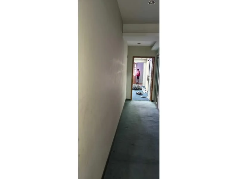 Room features: carpet flooring, plain white walls, ceiling lights, doorway leading to another room, narrow hallway, neutral color scheme.