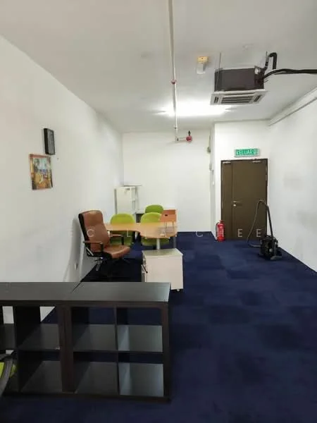 Room features: white painted walls, blue carpet flooring, 1 wall-mounted split AC, wooden desk, 4 green plastic chairs, 1 brown leather office chair, black shelving unit, door with brown finish, fire extinguisher, wall-mounted artwork; style: modern.