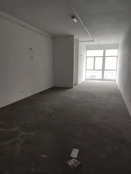 Room features: white painted walls, concrete flooring, large windows, exposed ceiling with light fixtures, empty space, no visible furniture, minimalist design, neutral color palette; style: minimalist; view: city.