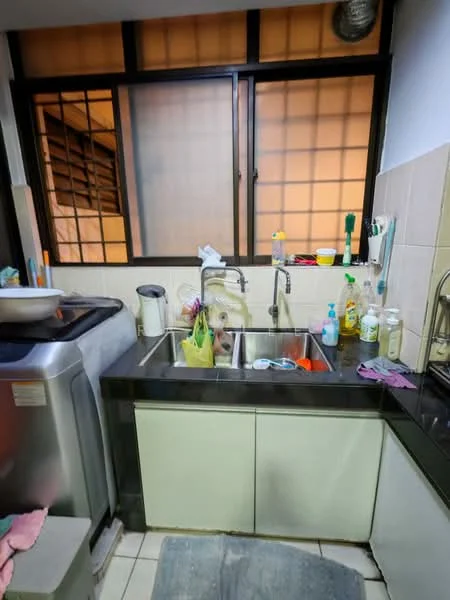 Kitchen features: single-bowl stainless-steel sink, chrome pull-down faucet, black countertop, white cabinetry, tile backsplash, built-in washing machine, window with grid pattern, various cleaning supplies, dish rack, floor tiles, kitchen mat.