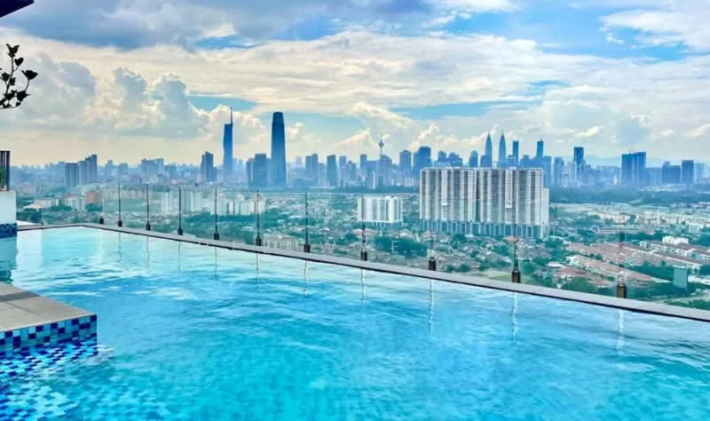 Exterior type: high-rise condominium; features: infinity pool, glass railing, city skyline view, tiled pool deck, surrounding urban landscape, cloudy sky, high-rise buildings in background; style: modern.