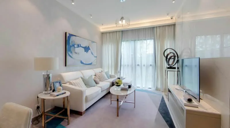 Living features: white fabric 3-seater sofa, glass coffee table with metal legs, wall-mounted TV, light-colored carpet, floor-to-ceiling windows, sheer curtains, decorative sculpture, framed artwork on wall, recessed downlights, neutral painted walls, light wood flooring; style: modern.