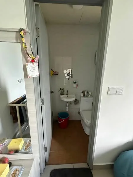 Bathroom features: white walls, brown tile flooring, toilet, sink, mirror, shower area, wall-mounted faucet, storage shelves, cleaning supplies, red bucket.