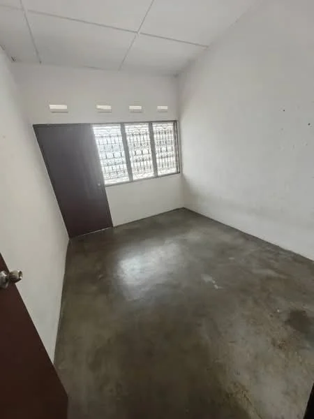 Room features: white painted walls, concrete flooring, single wooden door, metal window grills, three small windows, plain ceiling, no visible lighting fixtures; style: minimalist.