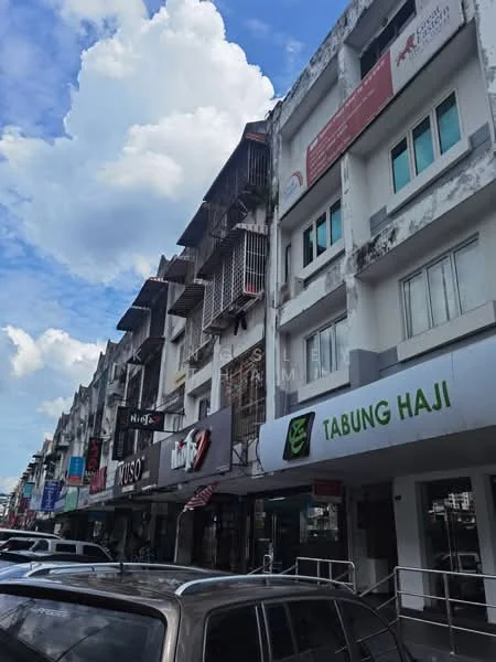 Exterior type: shophouse; features: multi-storey building, commercial signage, balconies with metal railings, white painted facade, glass windows, awnings over storefronts, street-level parking, urban context with nearby vehicles, cloudy sky, visible storefronts; style: modern.