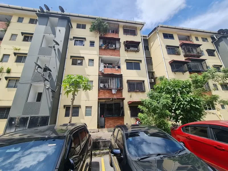 Exterior type: low-rise apartment block; features: yellow painted facade, brick accents, balconies with metal railings, multiple windows, satellite dishes on facade, surrounding greenery, parking area in front, two visible parked cars; style: modern.