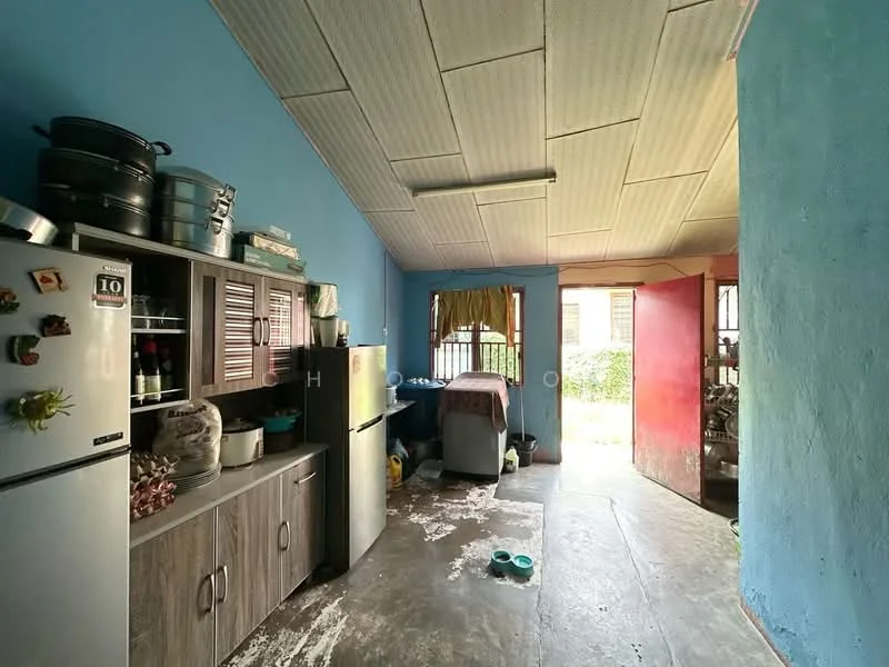 Kitchen features: blue painted walls, grey laminate cabinetry, stainless-steel fridge, countertop with sink, kitchen table, flooring with grey tiles, window with yellow curtains, exposed ceiling, light fixture on ceiling, open layout to adjacent room; view: garden.