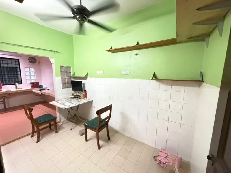 Room features: green painted walls, white tiled wall, ceiling fan, table with patterned surface, two wooden chairs with green upholstery, open shelving, tile flooring, staircase visible in background.