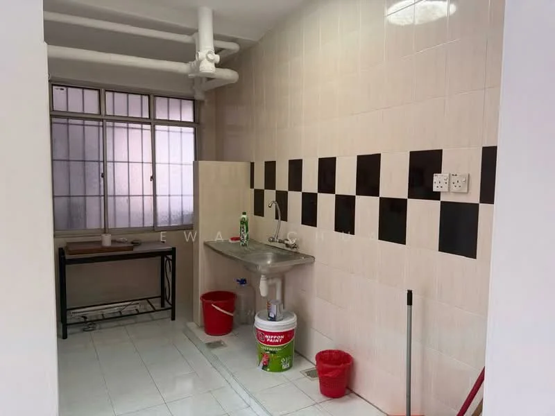 Laundry features: white tiled walls, black and white checkered backsplash, white tiled flooring, single-bowl stainless-steel sink, metal faucet, window with grid pattern, wooden table, two red plastic bins, cleaning supplies, exposed plumbing.