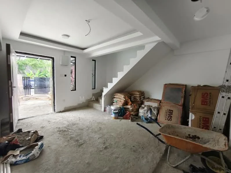 Room features: unfinished concrete flooring, white painted walls, exposed ceiling with recessed lighting, staircase leading to upper floor, large window with view to outdoor area, door leading to outdoor area, storage bags stacked against wall, wheelbarrow, construction materials visible.