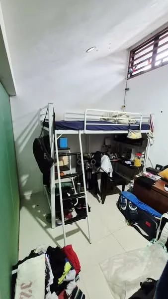 Room features: bunk bed with metal frame, white bedding, wooden desk, plastic storage bins, clothes on the floor, green wall, white tiled flooring, window with wooden slats, shelf unit, various bags and personal items.