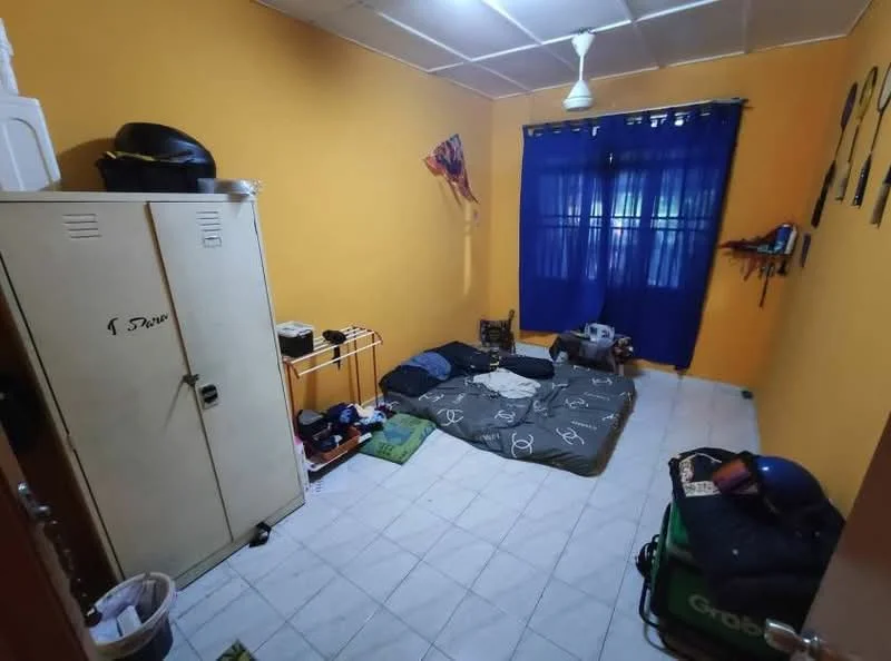Room features: orange painted walls, white ceiling, ceiling fan, blue curtains, tiled flooring, single bed mattress on floor, multiple cushions on floor, metal storage locker, wooden shelving unit, decorative wall hangings, waste bin.