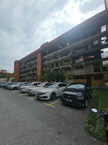 Exterior type: low-rise apartment block; features: 3-storey building, balconies on each floor, red brick facade, parking lot with marked spaces, multiple parked cars, surrounded by greenery, cloudy sky, sidewalk in front; style: modern.
