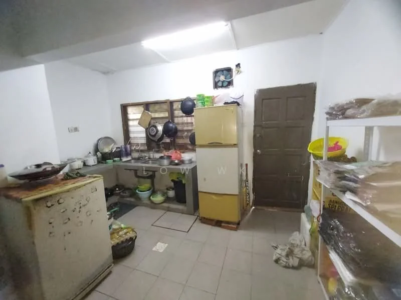 Kitchen features: white painted walls, grey tiled flooring, single-bowl stainless-steel sink, chrome pull-down faucet, freestanding fridge, built-in countertop with cabinets, wall-mounted shelves, various cooking utensils and pots, door leading to outside, window with metal grilles.