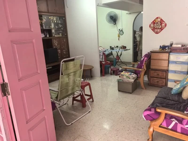 Living features: pink painted walls, tile flooring, ceiling fan, wooden coffee table, 2-seater wooden sofa, armchair with fabric upholstery, TV console, decorative wall art, open layout to adjacent room. Room features: folding table, plastic chairs, storage cabinet, decorative wall hanging.