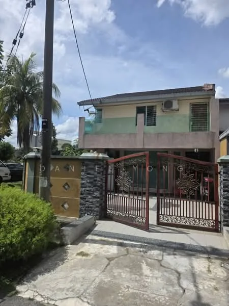 Exterior type: semi-detached house; features: two-storey structure, red metal gate, stone cladding on facade, green painted balcony, air conditioning unit visible, manicured hedge, paved driveway, palm tree in front yard, decorative wall with stone finish, clear blue sky; style: modern.