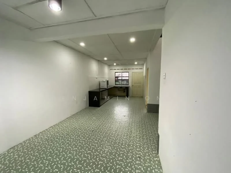 Room features: white painted walls, grey ceiling, recessed downlights, green patterned tile flooring, open layout, kitchen area visible, window with natural light, doorway leading to another room; style: minimalist.