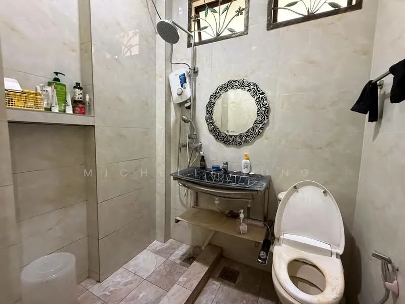 Bathroom features: shower with handheld shower head, wall-mounted shower mixer, framed round mirror, single-sink vanity with shelf, toilet, tile flooring, cream tiled walls, window with decorative grille, soap dispenser, toiletries on shelf, built-in shelving, white plastic bin; style: modern.