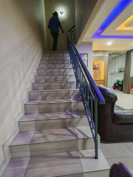 Room features: staircase with tiled steps, metal railing, wall-mounted light fixture, neutral wall color, recessed ceiling lights, decorative ceiling with blue LED lighting, open space at the top of the stairs, visible living area in the background; style: modern.