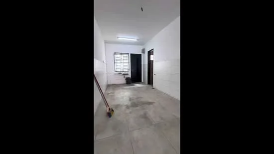 Room features: white painted walls, grey tiled flooring, window with horizontal slats, single door, ceiling light fixture, clean and empty space, mop or broom visible, corner with a waste bin; style: minimalist.