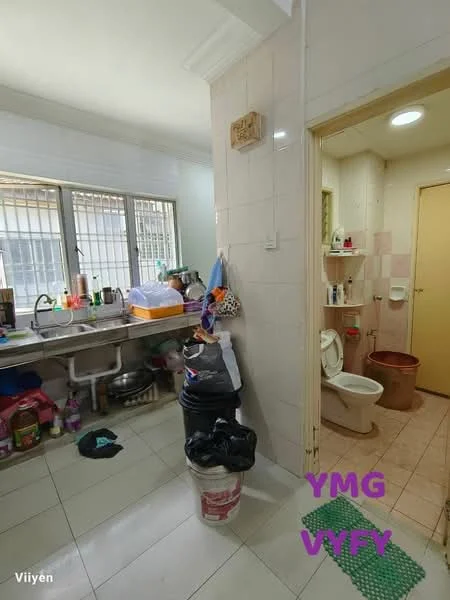 Room features: white tiled walls, light grey tiled flooring, single-bowl stainless-steel sink, wall-mounted cabinets, toilet, shelf with toiletries, plastic trash bin, various cleaning supplies, window with metal grilles, door leading to another room.