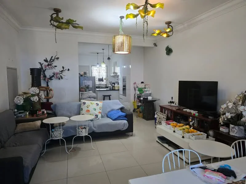 Living features: grey fabric sofa, blue throw blanket, 2 white side tables, wooden TV console, wall-mounted TV, decorative plants on wall, hanging light fixtures, white tiled flooring, crown moulding on ceiling, decorative wall art, fruit bowl on table, open layout to kitchen, dining table with white chairs; style: contemporary.